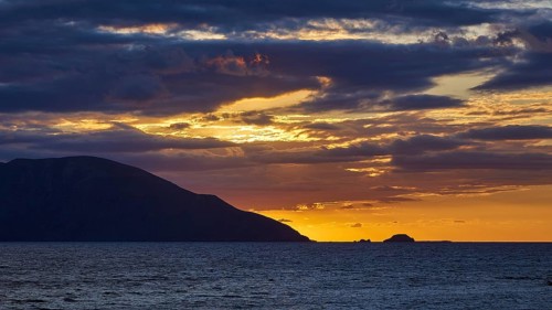 Sunset over the sea with dark clouds and silhouette of the mountains on the horizon, sunset,