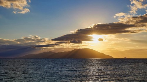 The sky shows a sunset over the sea with an island and clouds in the background, sunset, Kassos,