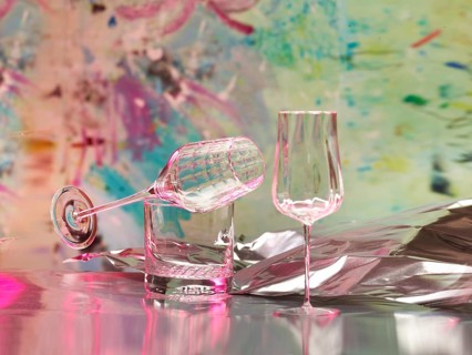 Various glasses on silver foil, behind them various splashes of colour, studio shot