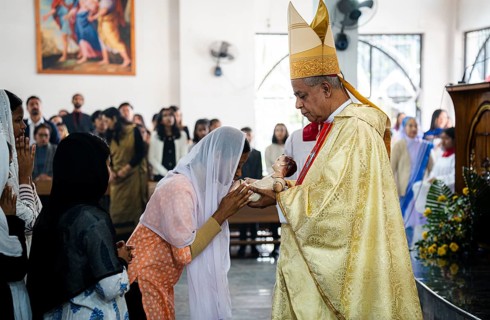 Archbishop John Moolachira holds an idol of baby Jesus Christ as devotees kiss the idol during a