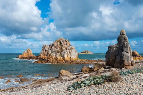 Rough coastal landscape with large rocks and calm sea under a cloudy sky, Plage de Pors Scaff,