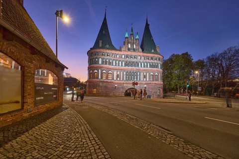 City gate Lübeck Holstentor, historic brick building, footpath and cycle path, evening blue hour,