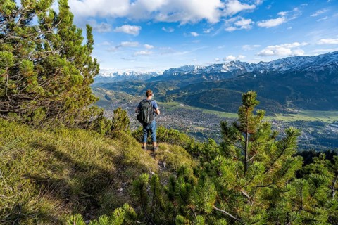 Mountaineer on a narrow hiking trail between mountain pines, view of Garmisch-Partenkirchen and