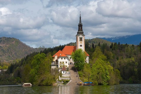 Church on a green island in the lake, framed by wooded mountains, Bled Island with St Mary's