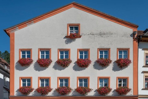 Residential building façade with blooming geraniums (Pelargonium) in the flower boxes at the