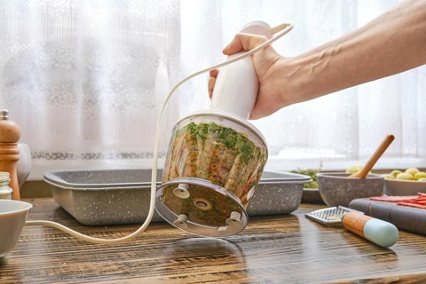 A hand blender is being used to create a fresh vegetable puree in a well-lit kitchen. Ingredients