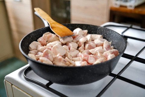 Cooking chunks of chicken in a black skillet over a gas stovetop. The cozy kitchen environment