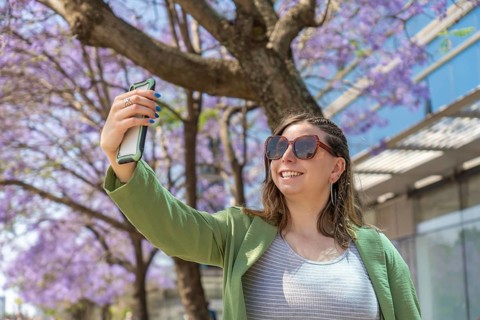 Smiling businesswoman taking a selfie with smartphone in a city street with blooming jacaranda