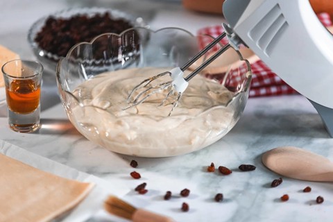 An electric mixer stirs cream of curd cheese, rum and sultanas next to it