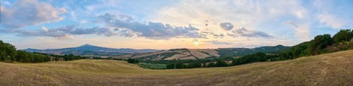 Typical Tuscan landscape in Val d'Orcia with hills, trees, fields, cypresses and farm road in