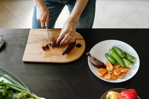 Close-up of female hands chopping fresh baby beetroot on wooden board