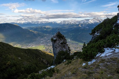 Rocky peak with summit cross, view of Garmisch-Partenkirchen and mountain panorama, hike to