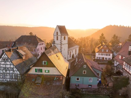 Church and half-timbered houses in a village in the evening light, surrounded by forest and idyll,