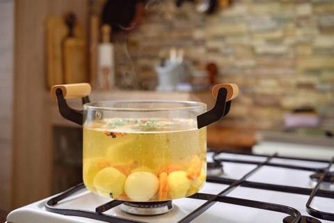 A clear pot filled with simmering vegetable broth sits on a gas stove, showcasing vibrant