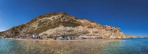 Rocky coastal landscape with Paralia Agios Theodoros sandy beach and sunshades in front of a clear
