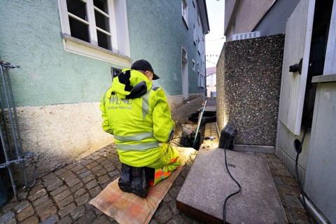 Worker in high-visibility clothing kneeling on cobblestones during construction work next to