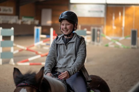 Laughing little girl, 10 years old, on a horse in an indoor riding arena, Mecklenburg-Vorpommern,