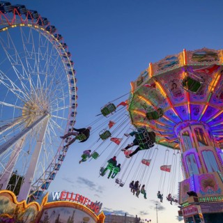A funfair at dusk with illuminated chain carousel and Ferris wheel, Europa Rad, rides, wave flight,