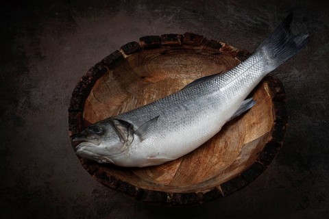 Fresh, raw sea bass fish, in a wooden plate, top view, no people