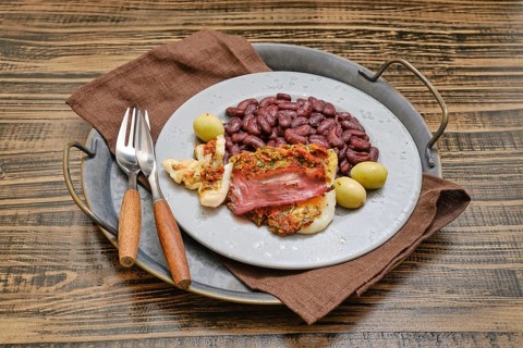 A plate showcases seasoned fish topped with ham, accompanied by red beans and green olives,
