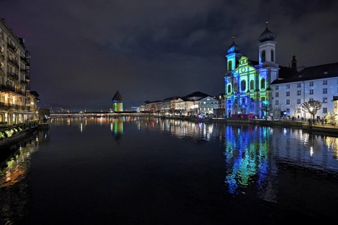 Water tower and Jesuit church on the right with light installation, on the Reuss at dusk, Old Town,