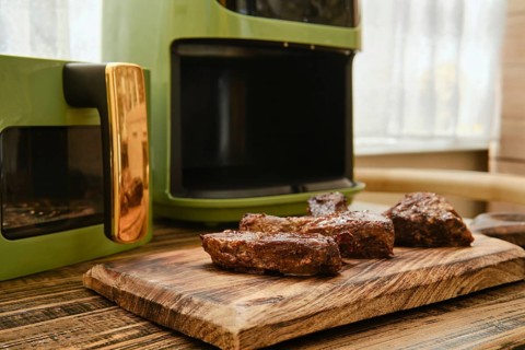Juicy pieces of meat rest on a wooden cutting board after being fried in modern air fryer