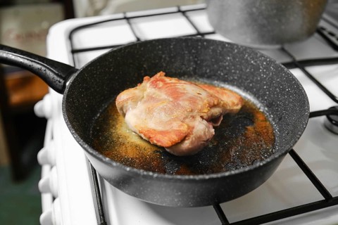 Juicy turkey meat sizzles in a black skillet placed on a gas stove in a cozy kitchen. The cooking