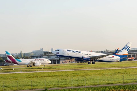 Two SunExpress and Eurowings aeroplanes at an airport. One takes off and the other approaches,