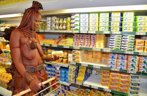 Traditionally dressed Himba woman holding a packet of butter, standing in front of the refrigerated