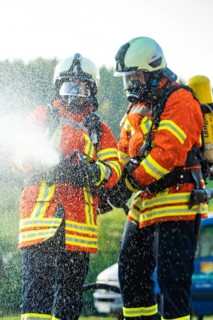 Two firefighters in full protective clothing spraying water with a fire hose, fire brigade,