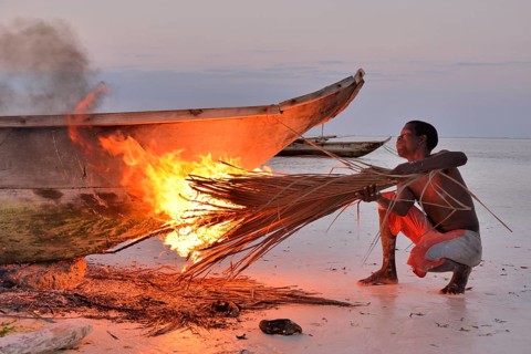 Fisherman smoking his boat with burning palm fronds, to harden the surface and to remove vermin,