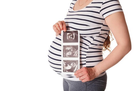 Pregnant woman standing and holding her ultrasound baby scan picture isolated on white