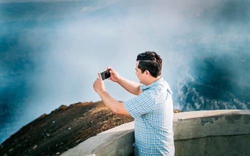 Joven turista tomando fotos en un mirador volcánico. Hombre aventurero con su celular tomando fotos