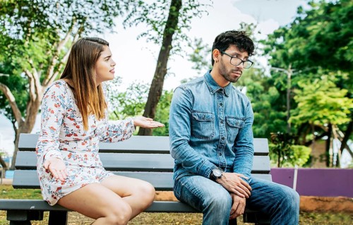 Upset couple arguing in a park. Girl arguing with her boyfriend sitting in a park, Young couple
