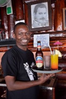 Waiter with Kilimanjaro beer and a cocktail in front of a picture of Freddy Mercury, the late