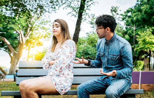 Man arguing with his girlfriend sitting in a park. Upset couple arguing in a park. A young couple