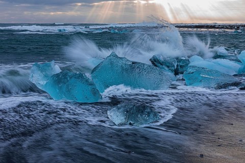 Waves breaking on icebergs on the black beach of Breidamerkursandur, near Jökullsarlon, Sudurland,