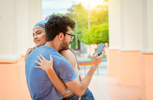 Unfaithful boyfriend hugging his girlfriend and looking at the cell phone. Concept of unfaithful