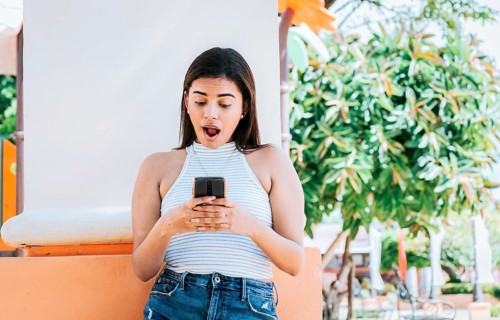 Surprised person looking at cell phone outdoor. Girl with cell phone with a surprised face leaning