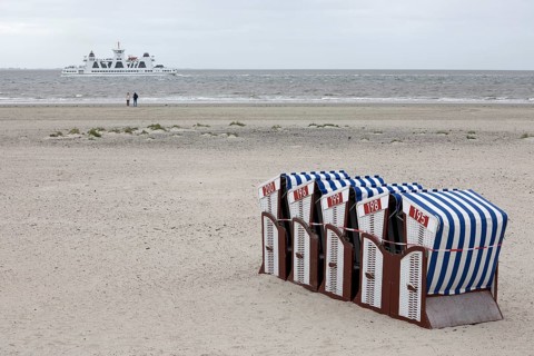Beach chairs tied together on the beach with only two people on the water and ferry departing, end