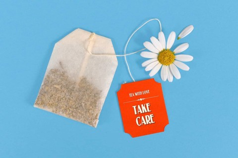 Tea bag with made up cute red label with text Take care with daisy flower on blue background