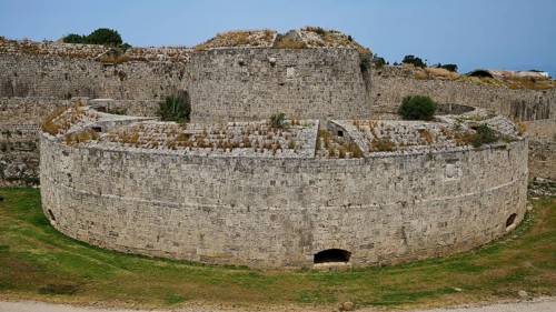 Fortress wall, Bastion del Carretto, A massive, round stone fortress rises on a green meadow, an