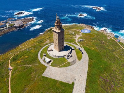 Majestic lighthouse on the coast with green grass and deep blue sea under a bright blue sky, aerial