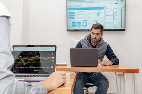 A middle-aged man is deeply focused on his laptop in a modern coworking space, with a screen