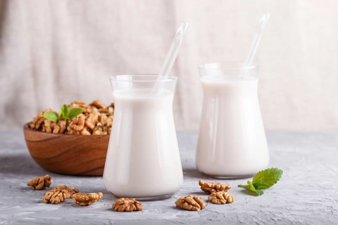 Organic non dairy walnut milk in glass and wooden plate with walnuts on a gray concrete background.