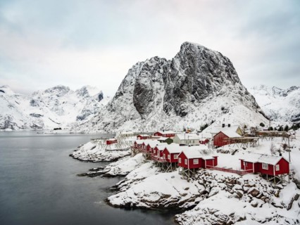Rorbuer huts of Hamnoy at the fjord, snowy mountains in the background, Hamnøy, Reine, Moskenesøya,