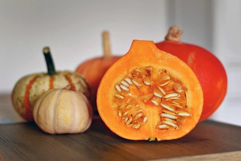 Halved Hokkaido pumpkin showing seed on cutting board with other pumpkins in background