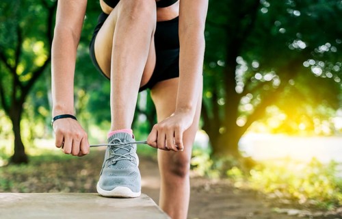 Close-up of sporty woman tying her shoes. Athletic girl tying her shoe laces in a park. Runner girl