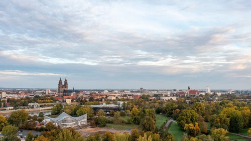 Autumnal deciduous trees in the Rotehorn municipal park, behind them listed hypar shell, Magdeburg