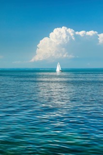 White sailboat on the turquoise water of Lake Constance with a low, large spring cloud in the